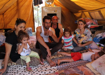 Zwei Männer, zwei Frauen und drei Kinder sitzen in einem Zelt.
