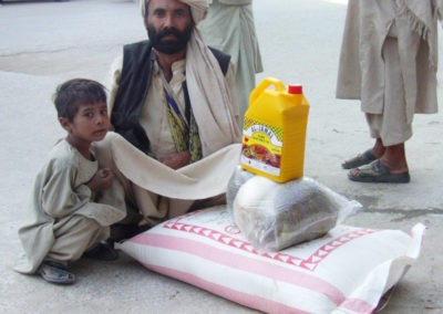 Ein kleiner Junge hockt mit einem Mann mit Turban vor einigen Grundnahrungsmitteln