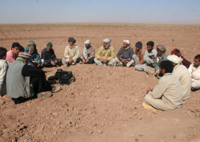 Eine Gruppe von Männern sitzt in einem Halbkreis auf einem Acker.