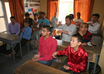 Männer und Jungen sitzen in einem Klassenraum auf Schulbänken.