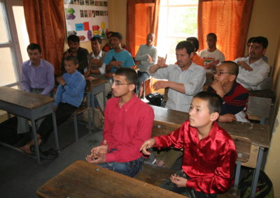 Männer und Jungen sitzen in einem Klassenraum auf Schulbänken.