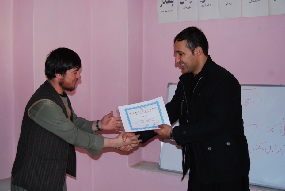 Ein Ausbilder überreicht einem Absolventen ein Zertifikat.
