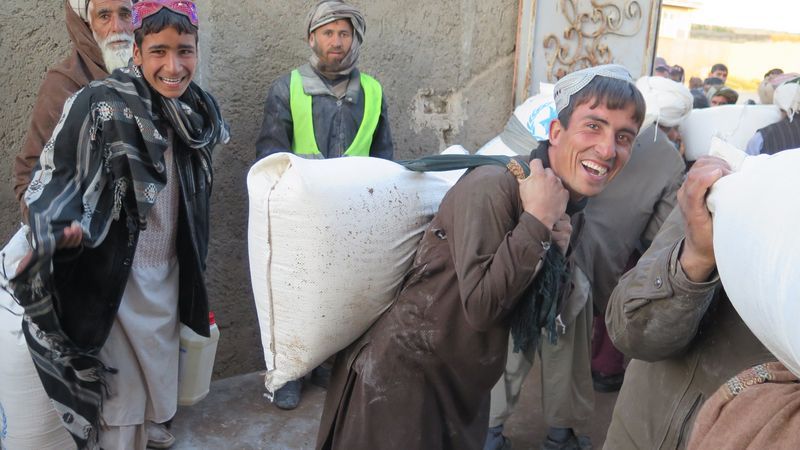 Un hombre con vestimenta tradicional afgana lleva un saco de harina al hombro.